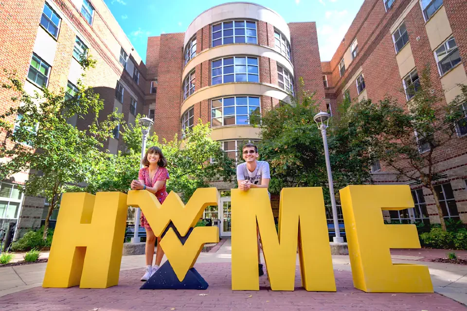 Two students pose with the Flying WV logo and giant HOME letters outside Honors Hall