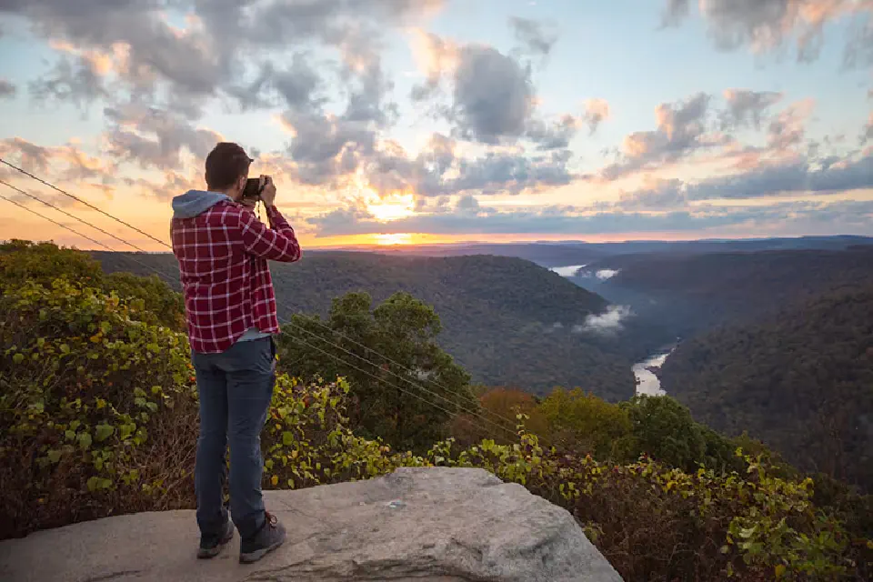 A person photographs a beautiful sunrise view of the Cheat River canyon.