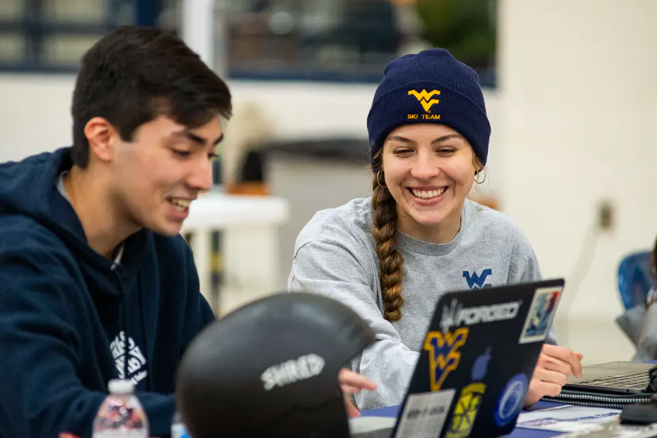 Two students working at laptops at their table for the WVU Student Org Fair.