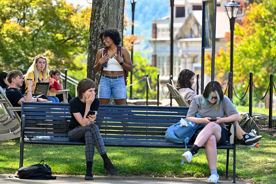 A group of people have a casual conversation while standing in Woodburn Circle. WVU's iconic Woodburn hall and a Let's Go flag is in the background.