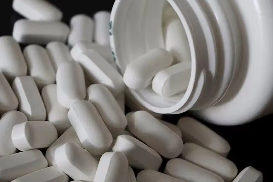 Oblong white tablets spill out of bottle