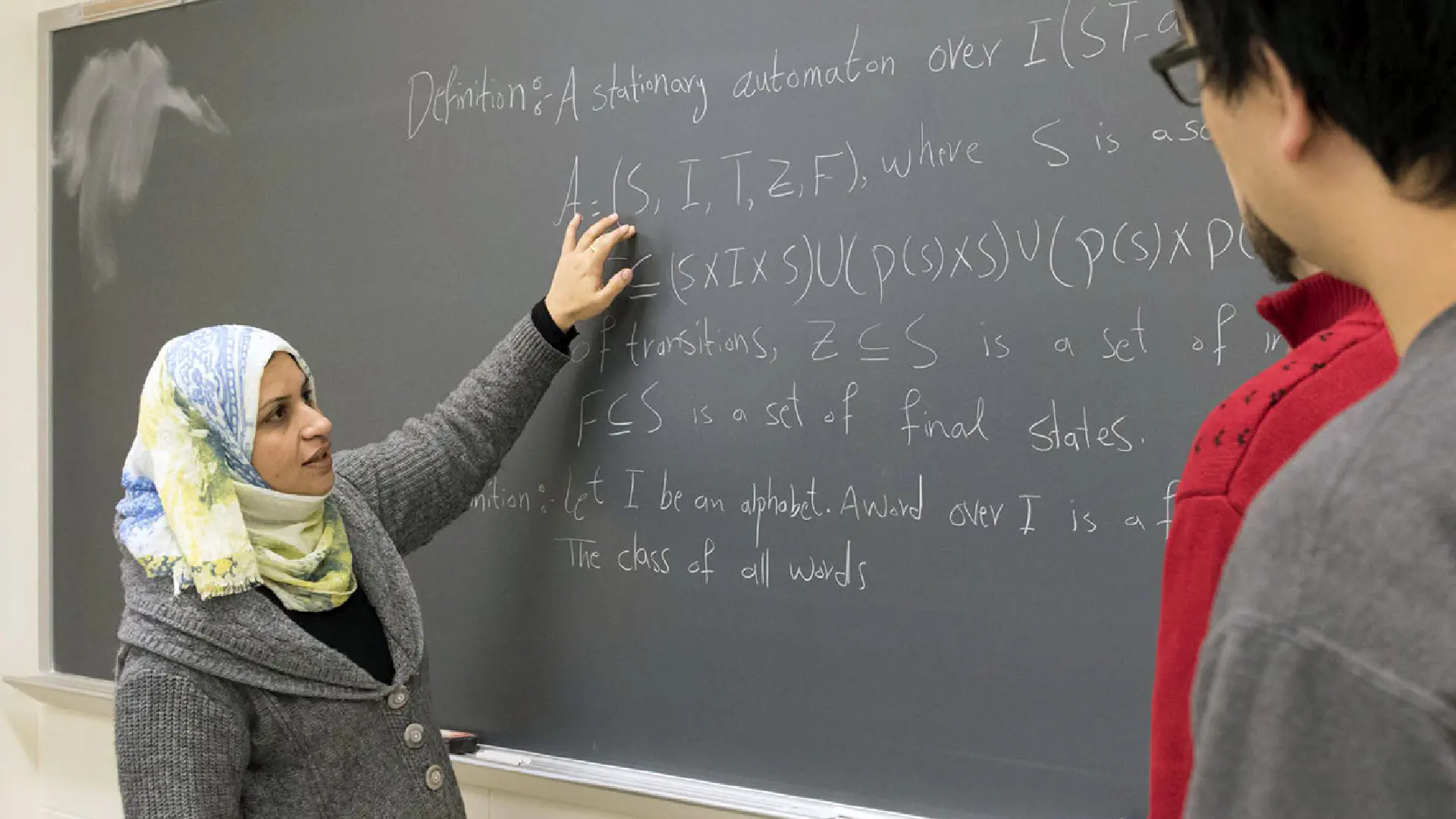 People studying math formulas written on a blackboard