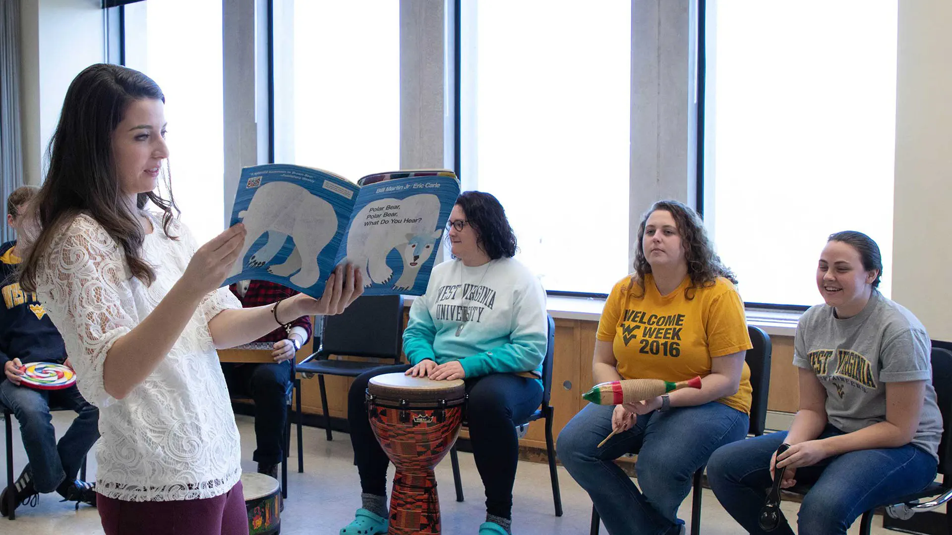 Person holds up a children's book while speaking to the class.