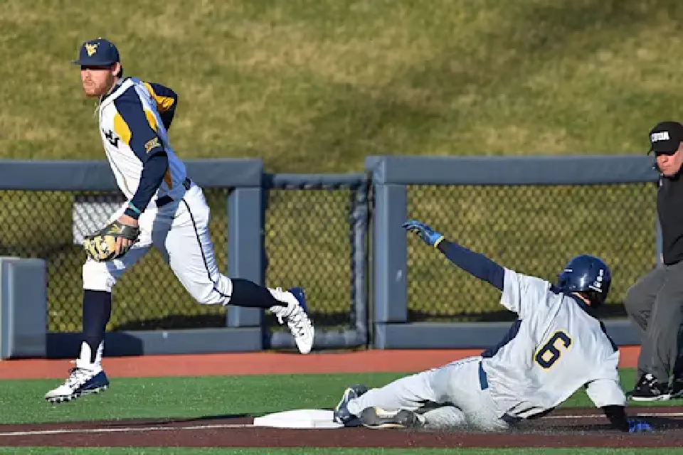 An player slides into base as a Mountaineer baseball player prepares to throw the ball