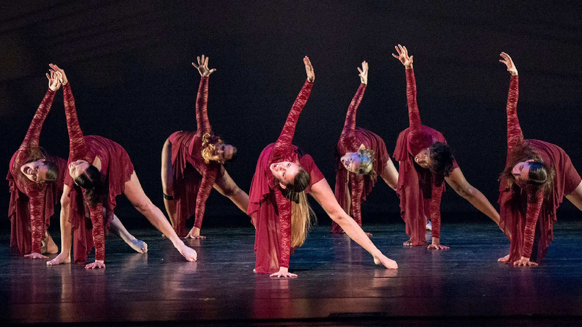 In unison, a group of dancers touches the stage with one hand reach toward the sky with their other hand