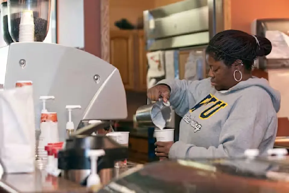 A student worker pours milk into a cup.