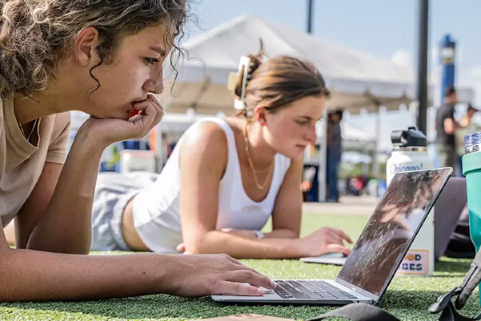 Two students use computers on the Mountainlair Green on a warm, bright day.