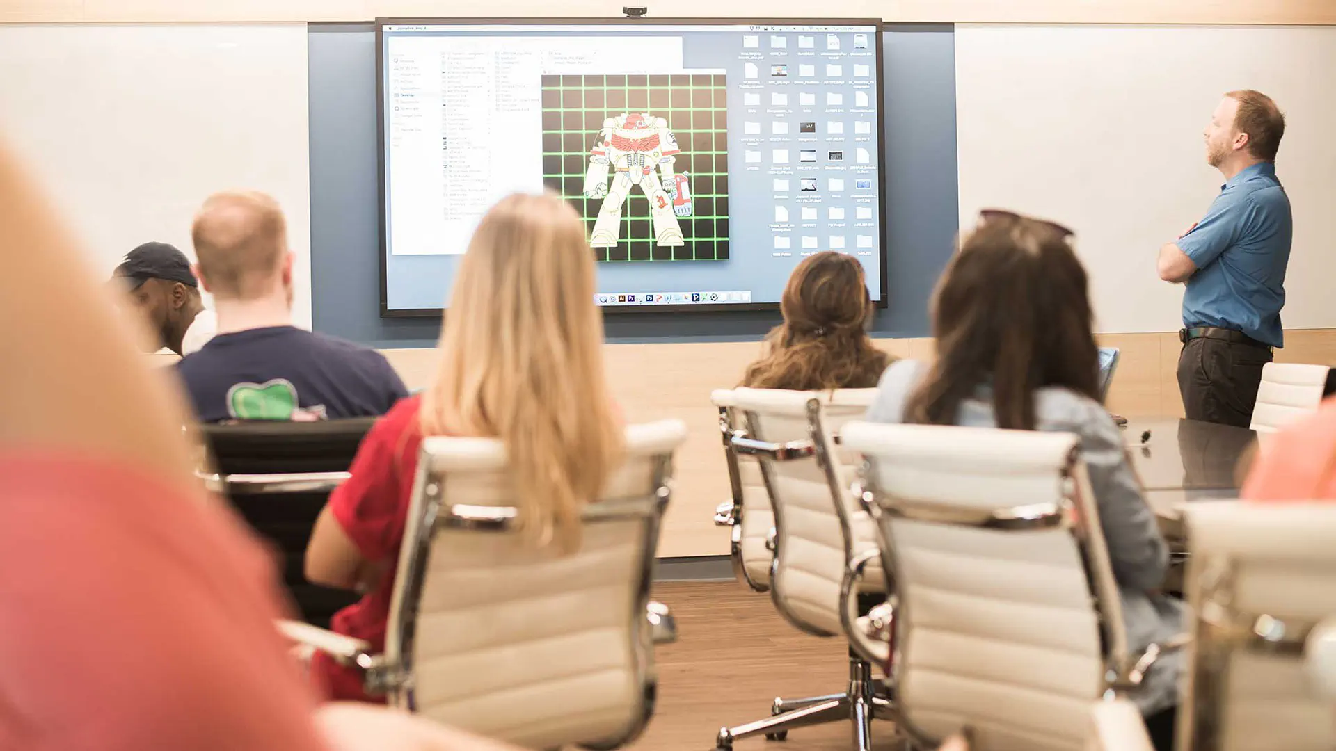 Students and professor view a student's design on the classroom screen.