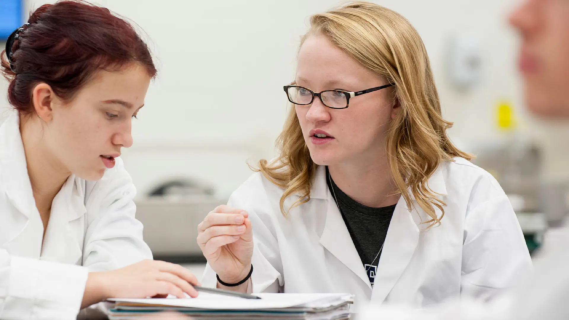 Two students in lab coats reviewing notes