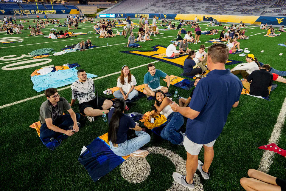 A large group of students sit on the green at Milan Puskar Stadium.