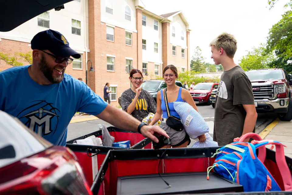 A student receives help with moving into their residence hall from their family .