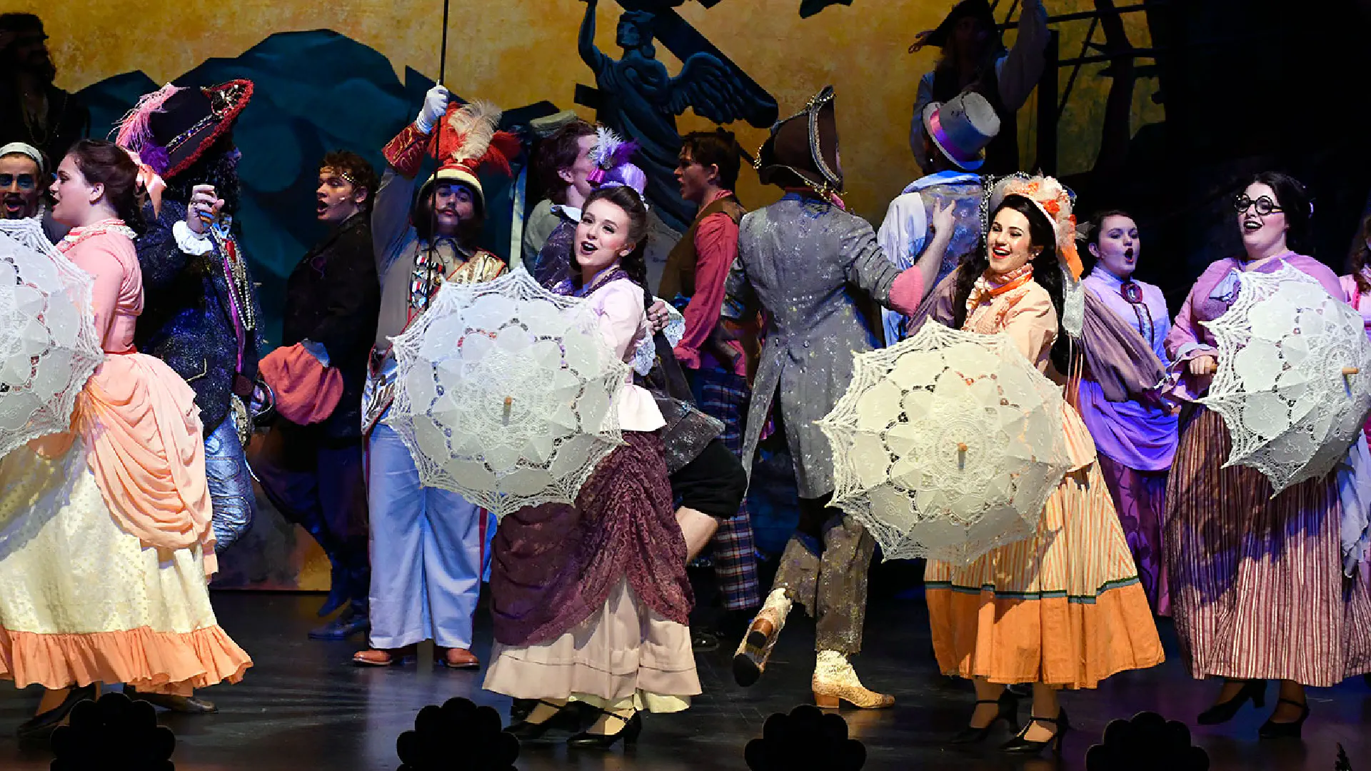 Costumed performers carrying umbrellas dance on stage