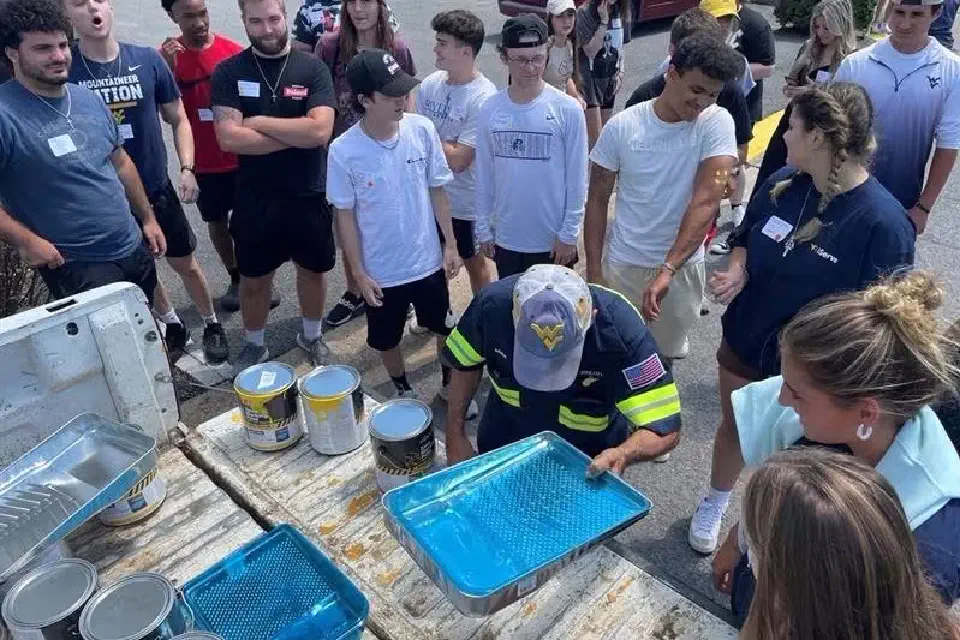 Students gather around a community worker pouring paint into trays