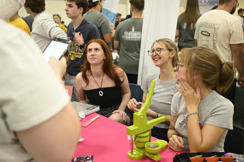 Three students sitting at their Student Organization Fair table converse with a attendee.