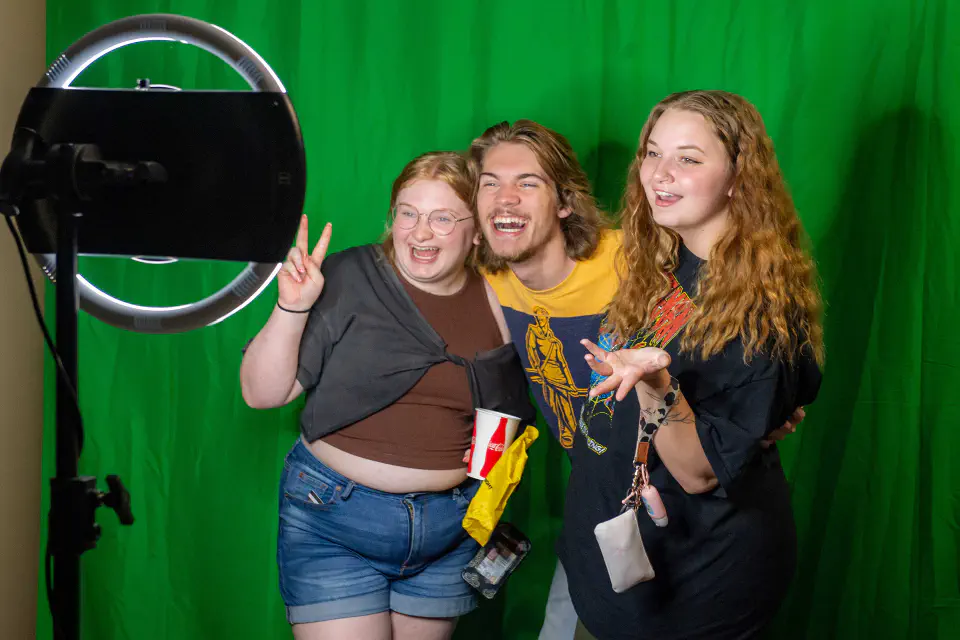 Three students pose for a photo in front of a greenscreen at WVUp All Night.